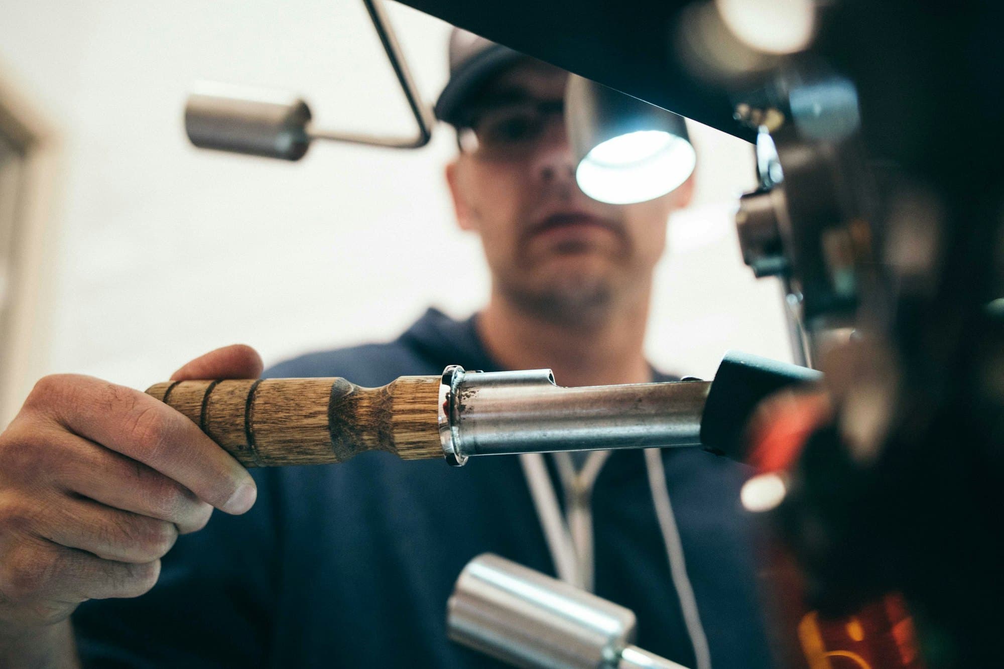 Artisan serrurier au travail : main tenant un outil de précision, lampe frontale, établi.